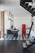 Offener Wohnraum mit Küchenblock unter Deckenleuchten in Gruppe und roter Fifty Kühlschrank auf schwarz weißem Boden, teilweise sichtbare Treppe im Vordergrund auf dunklem Holzboden