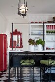 Bar stools with wrought iron and green seat cushions in front of breakfast bar; mirror with red, ornate frame and white, glass-fronted cabinet in background