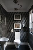 Guest toilet with grey optical art wallpaper and framed pictures; white pedestal toilet with cistern and pedestal washbasin to one side