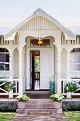Traditional white wooden house - veranda with turned columns and plant pots on steps leading to half-open front door