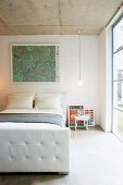 Framed map above French bed in simple bedroom with glass wall