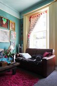 Dog sleeping on leather sofa in front of tall period window, gallery of artworks on turquoise wall