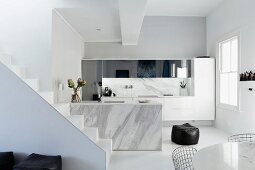 White staircase in front of marble kitchen counter with sink; partially visible wire-framed chairs at round table in foreground