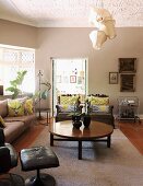 Round coffee table on pale rug and sofa set in elegant living room; whimsical pendant lamp with traditional fabric lampshades hanging from stucco ceiling