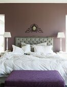 Elegant bedroom with upholstered headboard below hand-crafted ornament on wall painted pastel lilac