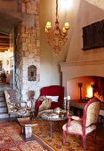 Various armchairs in cosy seating area next to open fire and doorway with stone column