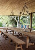 Pleasant dining room with glass walls and rustic wooden furniture; wrought iron chandeliers suspended from ceiling