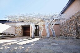 Four tree-shaped metal sculptures in courtyard with stone walls under blue sky