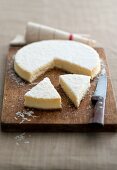 Cheesecake with grated coconut, partly sliced, on a chopping board