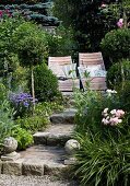 Weg mit Treppenstufen führt zu Liegestühlen in blühendem Garten
