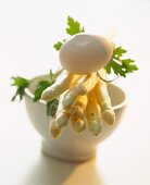 A still life of ingredients, featuring asparagus, an egg and a small soup bowl