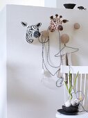 Papier mâché, hunting safari trophies and coat hooks on white wall and black bowls on wooden chair