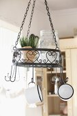 Pot of chives in wrought iron pendant basket with love heart motif and enamel mugs hanging from hooks
