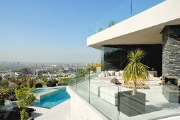 Zeitgenössisches Wohnhaus mit weissen Outdoormöbeln auf Terrasse und Glasbrüstung, im Hintergrund Pool und Stadtpanorama