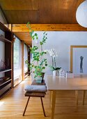 Holzbank mit Kissen und Blumentopf vor Tisch in offenem Wohnraum mit Holzdecke