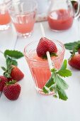 Strawberry juice with a strawberry on a skewer garnished with strawberry leaves
