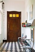 Various metal chairs against wall on chequered floor in foyer and old wooden door with square glass panels