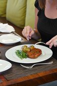 A woman eating a bacon wrapped meatloaf, herbed potatoes, green beans