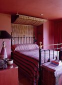 A bedroom in an English country house in shades of dark red with fabrics from Bhutan for the bed and canopy