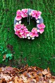Wreath of pink orchid flowers on mossy background above autumn leaves