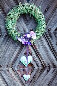 Willow wreath with purple flowers and decorative hearts on rustic front door
