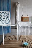 White metal chair with punched floral pattern on back next to retro radio on plexiglass table in shape of draped tablecloth