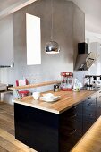 Black, glossy kitchen counter with breakfast bar and wooden worksurface in open-plan, attic interior