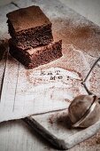 Drei kakaobestäubte Brownies auf weißem Zettel mit der Aufschrift Eat Me