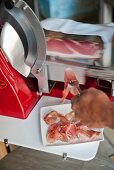 Prosciutto being sliced wafer thin by a slicing machine