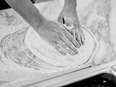 Hands brushing flour over pizza dough