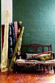 Bolts of patterned fabrics and wooden bench against brick wall painted petrol blue