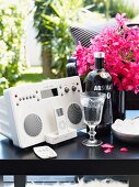 Stereo system and iPod next to liqueur glass and bottle of vodka in front of pink bouquet on black side table