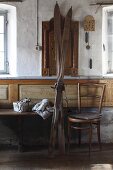 Vintage Skier neben Thonetstuhl vor Wand in karger Bauernstube, auf Sitzbank Weihnachtsgeschenk und Strickmütze