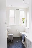 Plastic stool in front of sink, toilet and bathtub in bathroom with black mosaic floor tiles