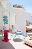 Terrassenbereich eines mediterranen weissen Wohnhauses mit Tisch & Stühlen aus Metall, Bodenkissen & Hängematte