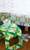 Gebogener Hocker aus Kunststoff mit grün-weiss gemustertem Stoff bezogen vor Bett mit floralem Muster