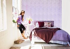 Sonniges Schlafzimmer mit verschiedenen Violetttönen auf Bettwäsche und grafisch gemusterter Wandtapete