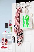 Printed cloth bag and scarf hanging on hooks with black knobs on open door and view of desk against wall painted pale blue