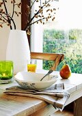 Bowl on linen napkin and white vase of flowering branches on wooden table