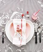 Romantic place setting with rose-patterned tablecloth, heart-shaped plate and sprig of pink flowers