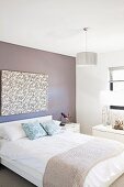 Doppelbett mit Tagesdecke vor hellgrau getönter Wand und modernem Bild in schlichtem Schlafzimmer