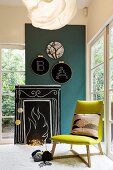 Hand-crafted, stylised open fire made from wooden board, blackboard paint, chalk and fairy lights in comfortable seating area with green chair and embroidery frames on wall