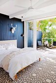 Schlafzimmer mit grafischem Teppichmuster, schwarzer Wandverkleidung und weißer stilisierter Trophäe vor Terrasse