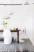 Dining area with white panton chairs and wooden table on patterned carpet in front of white wall covering