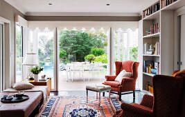 Living area with patterned, wing-back chair and Oriental rug in front of terrace doors