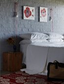 Double bed below red and white floral paintings and innovative sconce lamps on brick wall painted dark grey