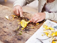 A girl cutting chanterelle mushrooms on a wooden table