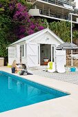 Weisses Strandhäuschen mit weitläufigem Holzdeck und angrenzendem Pool mit Mosaikfliesen