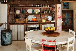 Obstschale auf rundem Tisch vor rustikaler Vintage-Küchenzeile mit offenem Wandregal