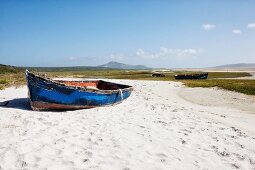 Simple boat with blue, peeling paint on sandy beach
